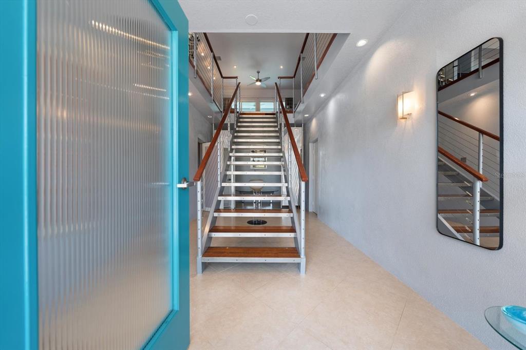 An entryway features a bright blue door, a modern staircase, and a wall-mounted mirror — 114 13TH STREET, BELLEAIR BEACH, FL