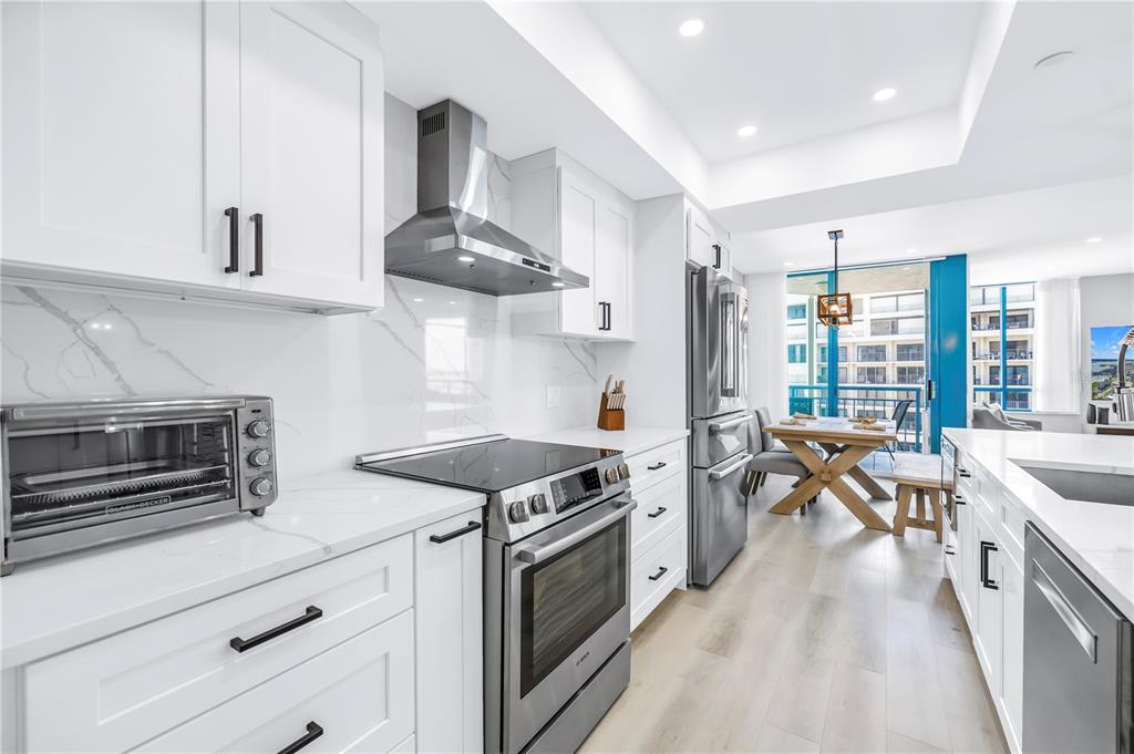 A modern white kitchen features stainless steel appliances, marble-style countertops, and an adjacent dining area — 1520R GULF BOULEVARD UNIT 906, CLEARWATER BEACH, FL
