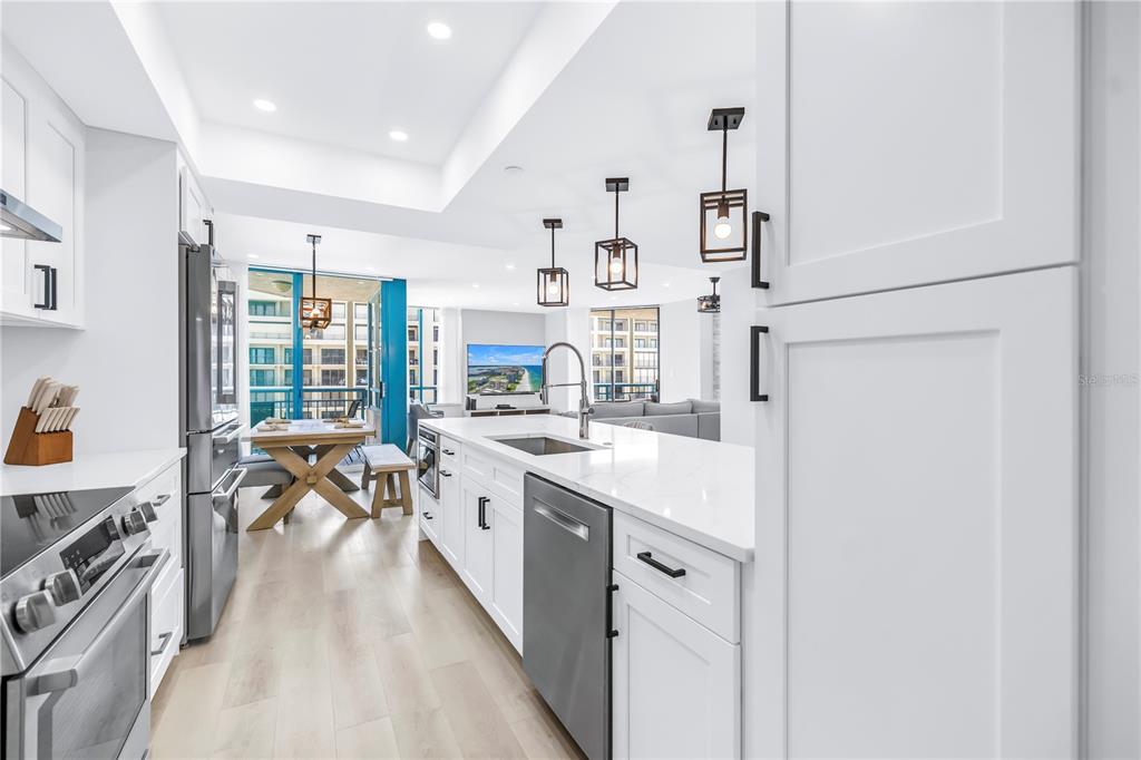 A modern white kitchen features a central island, stainless steel appliances, and an adjacent dining area — 1520R GULF BOULEVARD UNIT 906, CLEARWATER BEACH, FL