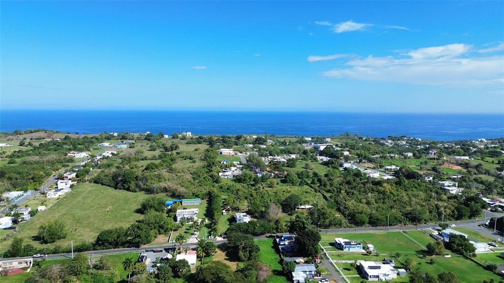 An aerial view shows a coastal landscape with scattered houses, green fields, and the ocean — 1117 CALLE VIRGINIA BARRETO GARCIA, QUEBRADILLAS, PR