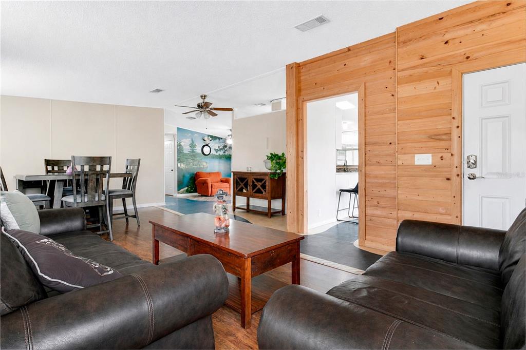 A living room with dark leather sofas, a wooden coffee table, and wood-paneled accent walls — 169 PINE TREE DRIVE, DEBARY, FL