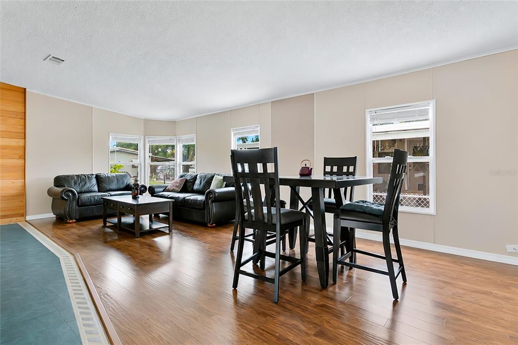 A living and dining area with wood flooring, black leather furniture, and a dark wood table — 169 PINE TREE DRIVE, DEBARY, FL