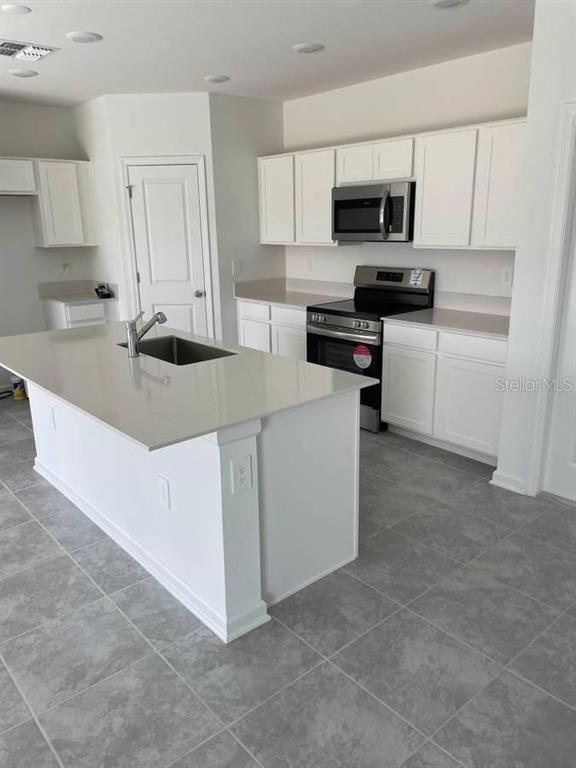 A kitchen features white cabinets, a central island with a sink, and stainless steel appliances — 1642 TEAGAN LANE, WINTER HAVEN, FL