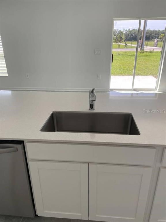 A kitchen island features a stainless steel undermount sink and white cabinets with quartz countertops — 1642 TEAGAN LANE, WINTER HAVEN, FL