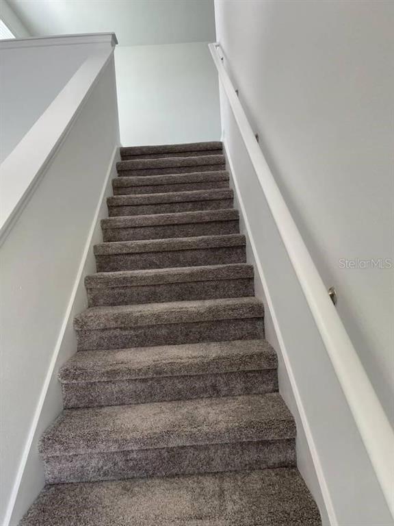 A straight staircase with gray carpeted steps and white walls leads to an upper landing — 1642 TEAGAN LANE, WINTER HAVEN, FL
