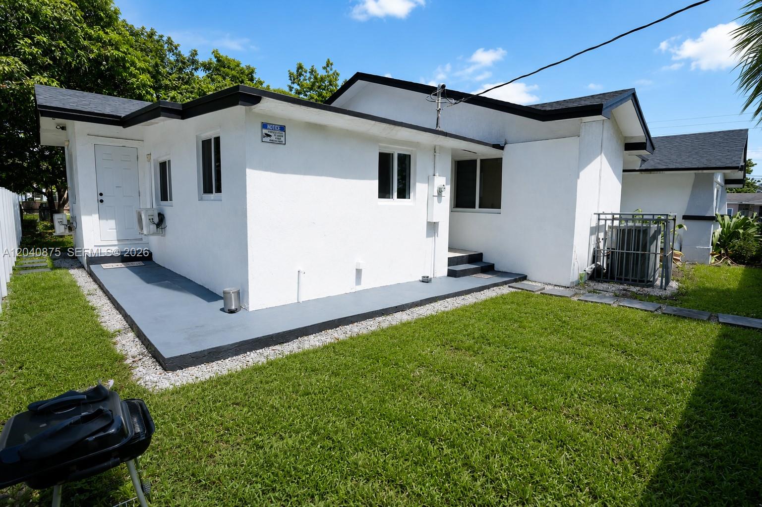 The exterior of a white house features a gray concrete patio and a grassy yard — 1860 NW 81st St, Miami FL 33147, MIAMI, FL