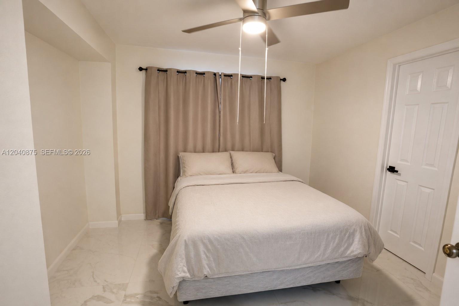 A bedroom features a bed with beige bedding, light-colored tile floors, and a ceiling fan — 1860 NW 81st St, Miami FL 33147, MIAMI, FL