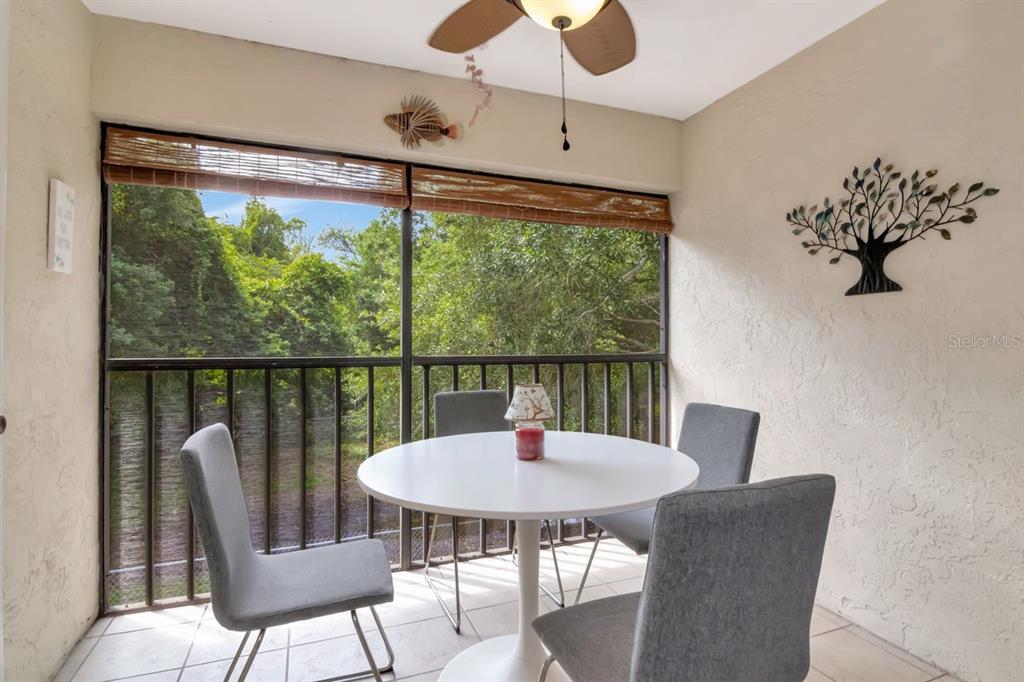 A screened-in balcony features a white round table, four gray chairs, and a nature view — 11511 113TH STREET UNIT 13F, LARGO, FL