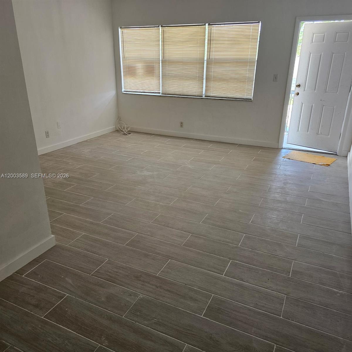 An empty room features light-colored wood-look tile flooring, white walls, and a white entry door — 230 SW 11th Ave # 14, Hallandale Beach FL 33009, HALLANDALE BEACH, FL