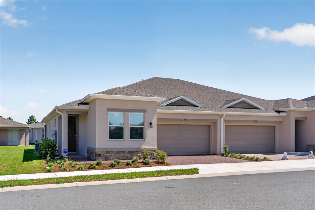 A tan stucco duplex with two garage doors and a stone-accented front exterior — 3231 NW 52ND AVENUE ROAD, OCALA, FL