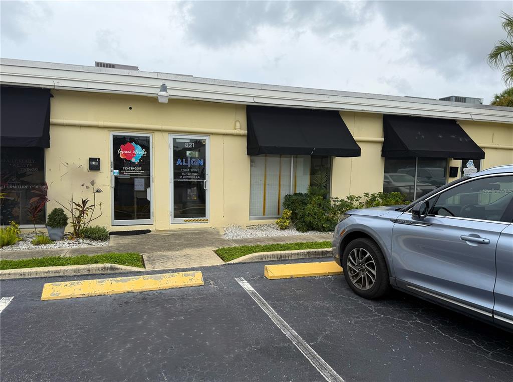 A single-story commercial building with black awnings, glass doors, and a parked silver car — 821 COURT STREET, CLEARWATER, FL