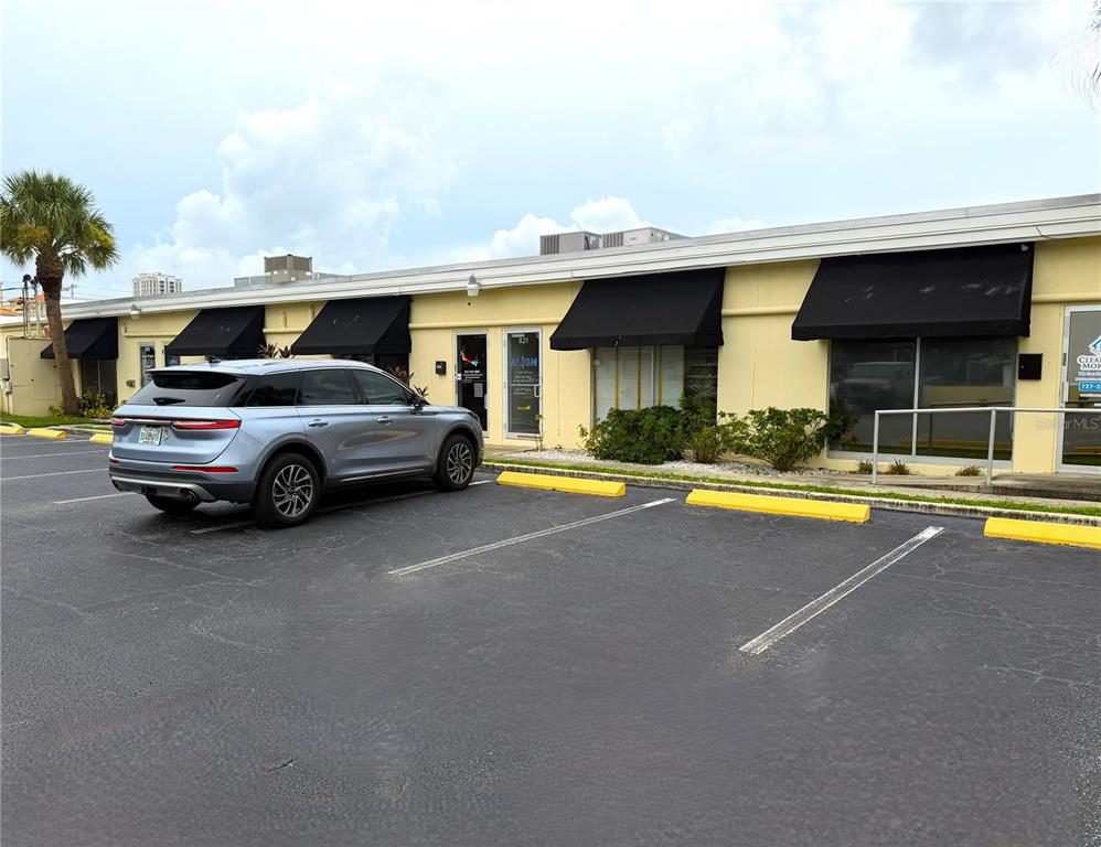 A light-colored commercial building with black awnings and a parked SUV in the parking lot — 821 COURT STREET, CLEARWATER, FL