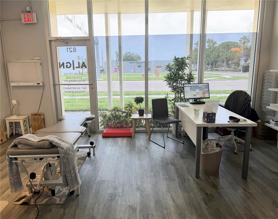 A small office space features a treatment table, a desk with a computer, and floor-to-ceiling windows — 821 COURT STREET, CLEARWATER, FL