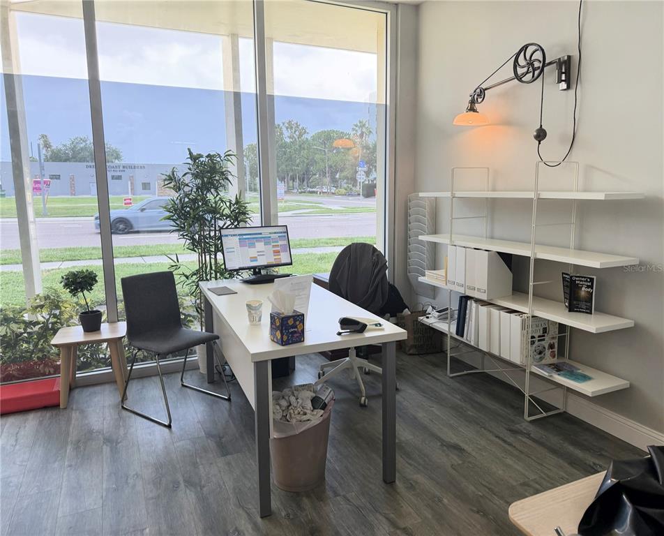 A bright office space features a desk, shelving unit, and large windows overlooking a street — 821 COURT STREET, CLEARWATER, FL