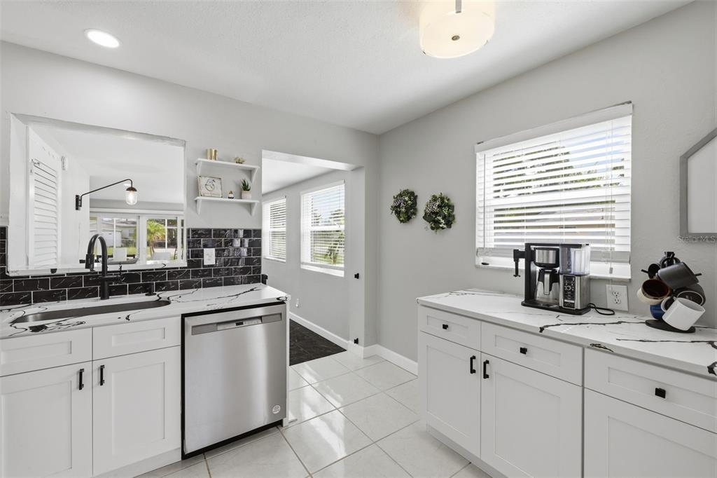 A kitchen features white cabinets, black and white marble-style countertops, and a stainless steel dishwasher — 801 89TH AVENUE N, ST PETERSBURG, FL