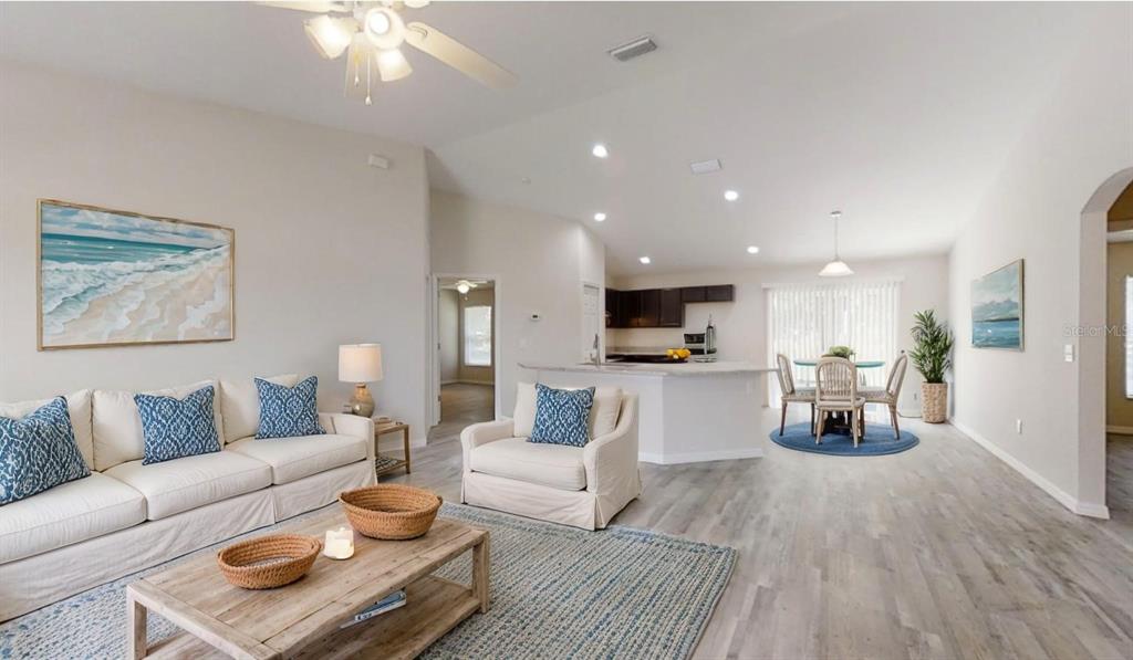 An open-concept living and dining area features light wood flooring, neutral walls, and modern furniture — 12966 SW 86TH COURT, OCALA, FL
