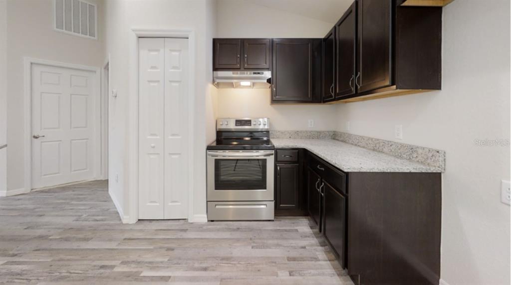 A kitchen features dark wood cabinets, granite countertops, stainless steel appliances, and wood-look flooring — 12966 SW 86TH COURT, OCALA, FL
