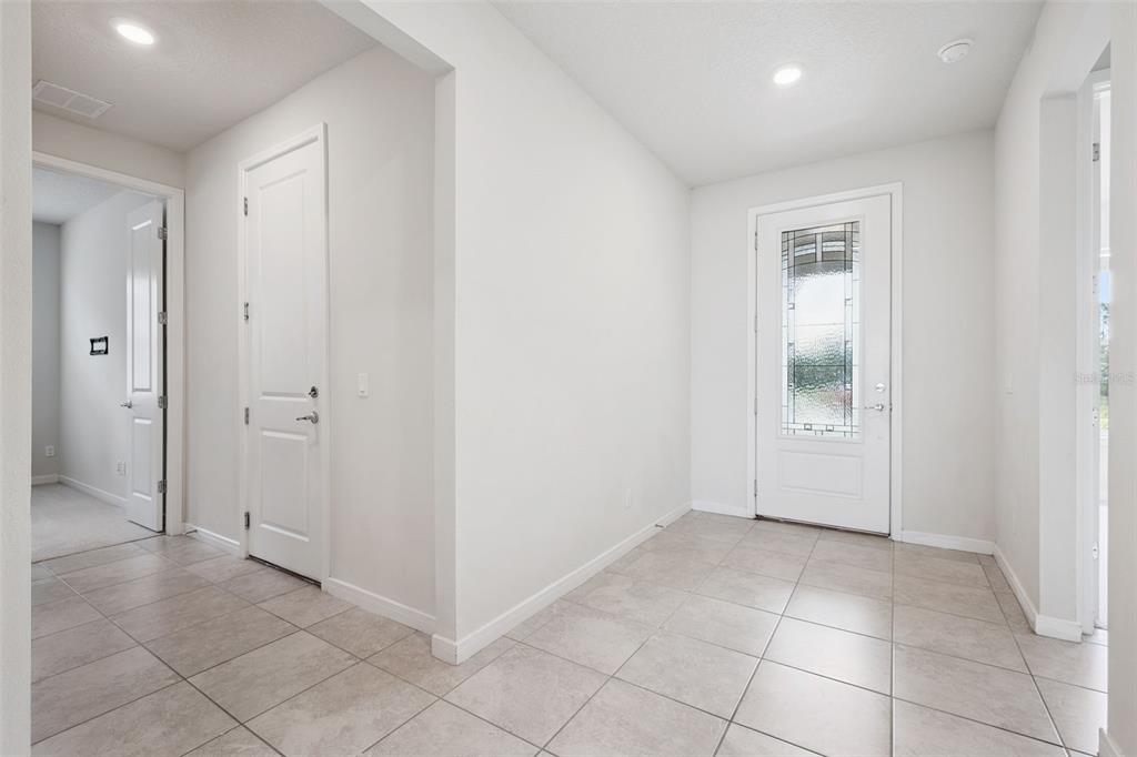 A bright entryway with light tile flooring, white walls, and a glass-paneled front door — 5668 ARBORVISTA STREET, ST CLOUD, FL