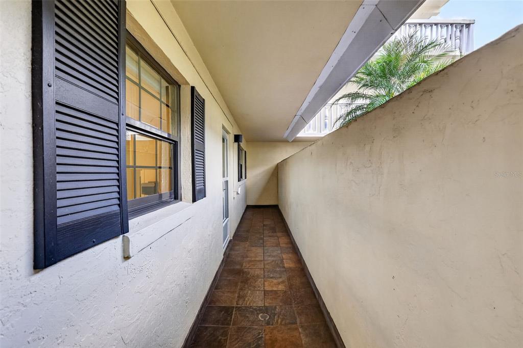 A narrow outdoor walkway features tiled flooring, a window with shutters, and a tall wall — 101 N GRANDVIEW STREET UNIT 1, MOUNT DORA, FL