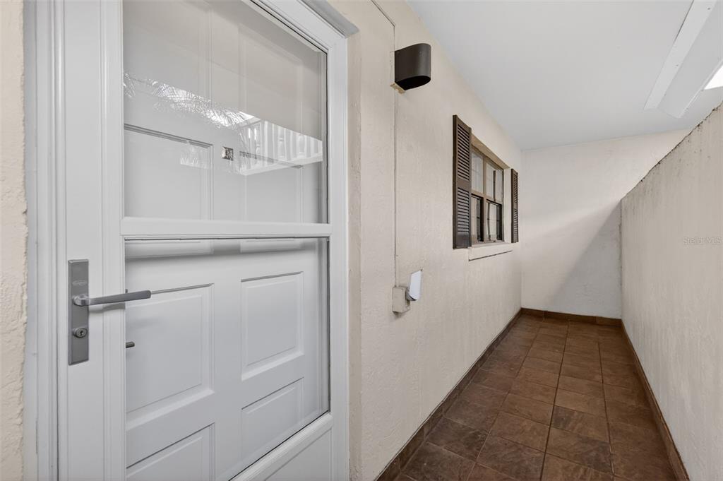 A narrow outdoor walkway features tiled flooring, a white door, and a window with shutters — 101 N GRANDVIEW STREET UNIT 1, MOUNT DORA, FL