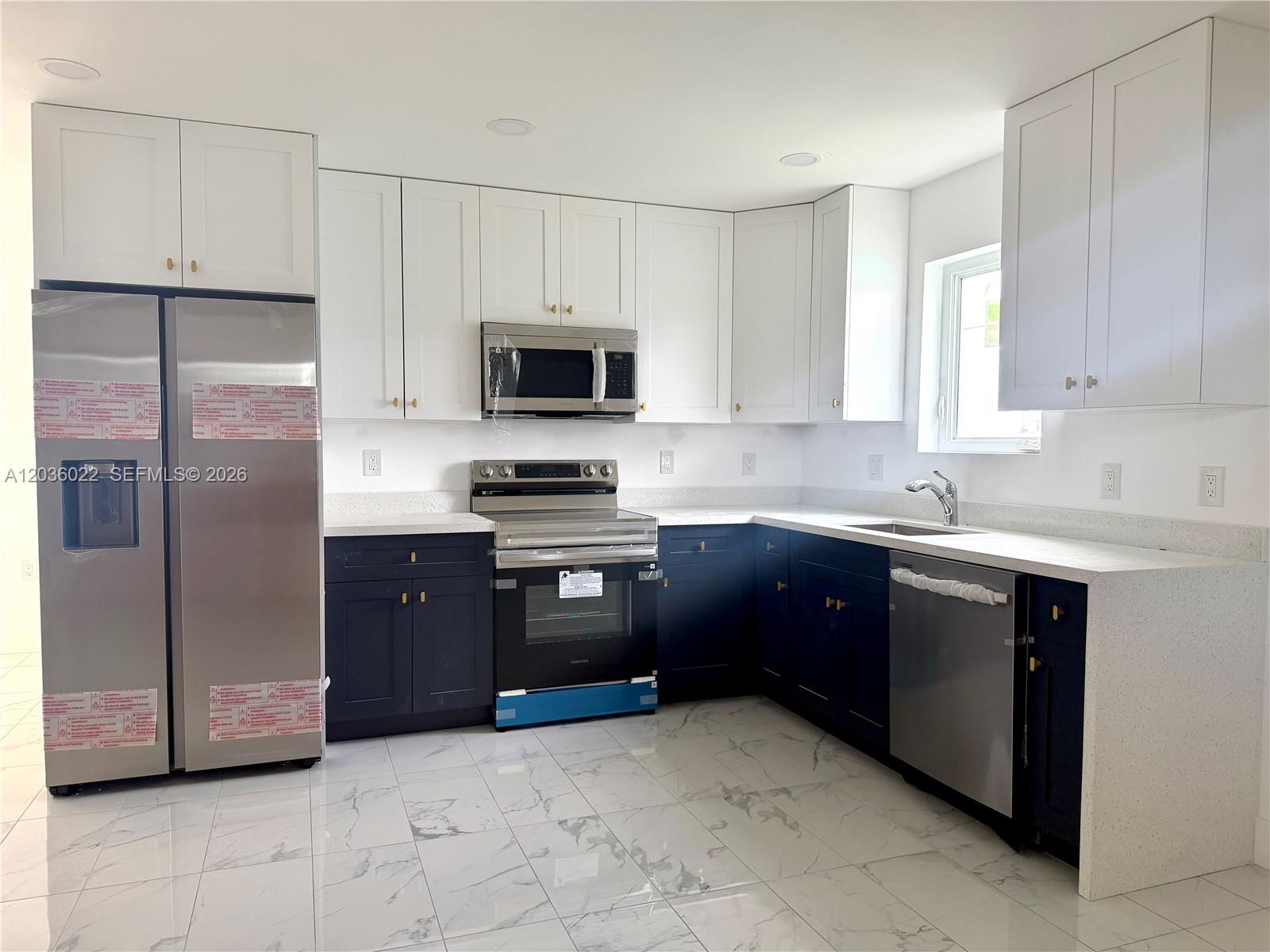 A kitchen features white upper cabinets, dark blue lower cabinets, stainless steel appliances, and marble-patterned flooring — 1629 NW 40th St, Miami FL 33142, MIAMI, FL