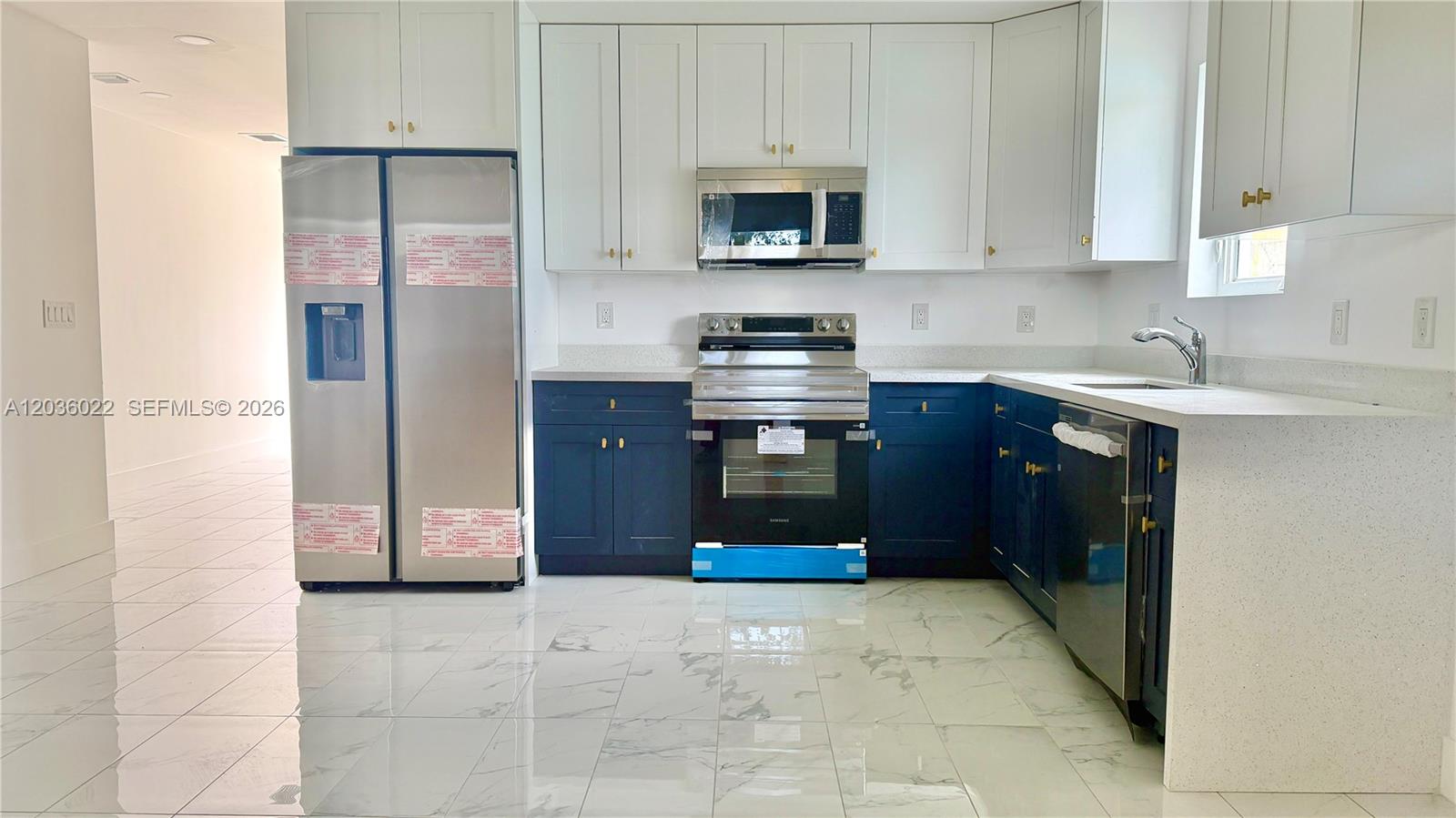 A kitchen features white upper cabinets, blue lower cabinets, stainless steel appliances, and marble-look flooring — 1629 NW 40th St, Miami FL 33142, MIAMI, FL