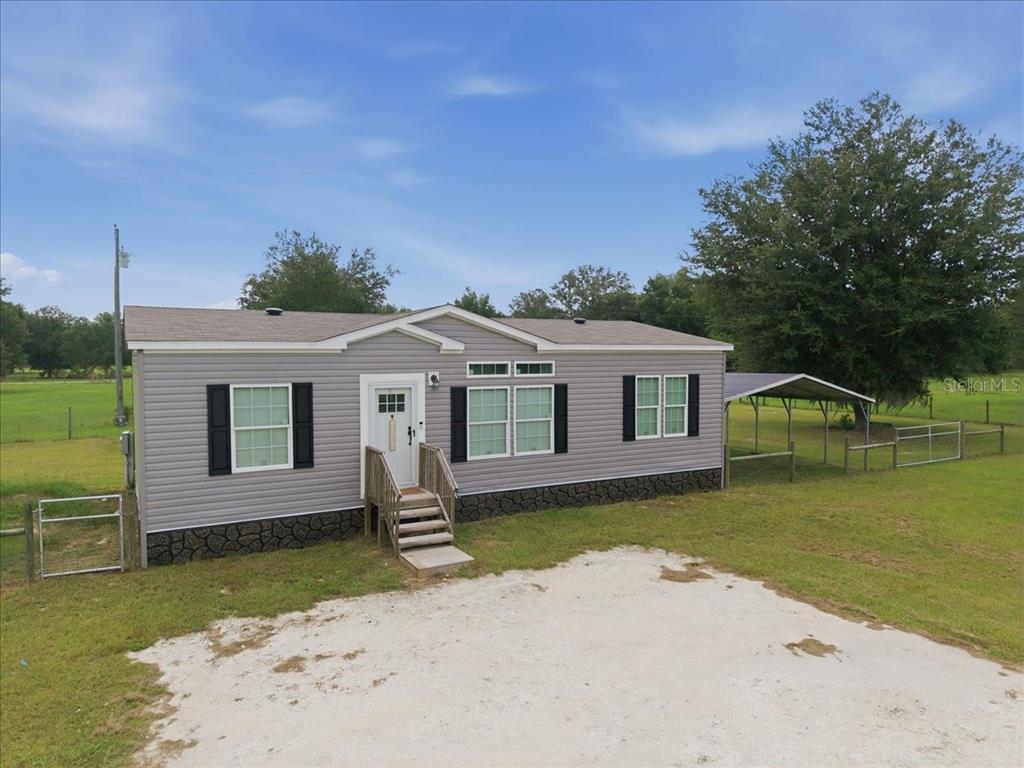 A gray manufactured home with a front porch, stone skirting, and an attached metal carport — 6731 CR 614, BUSHNELL, FL