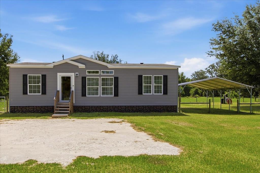 A gray manufactured home with a front porch and an attached metal carport on grass — 6731 CR 614, BUSHNELL, FL