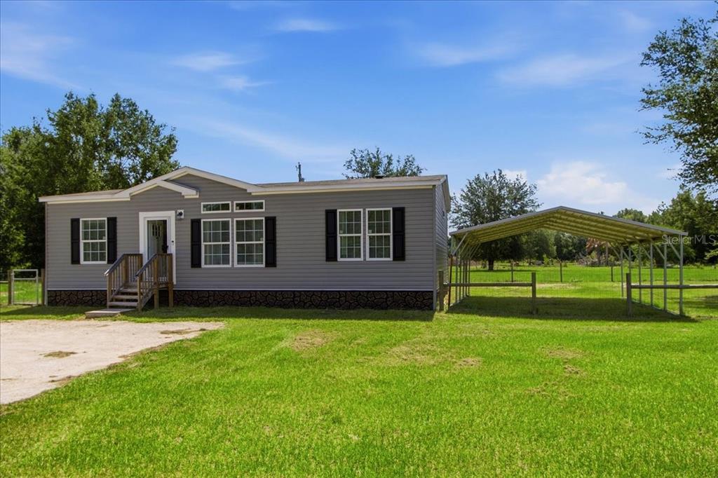 A gray manufactured home with a metal carport sits on a grassy lot — 6731 CR 614, BUSHNELL, FL