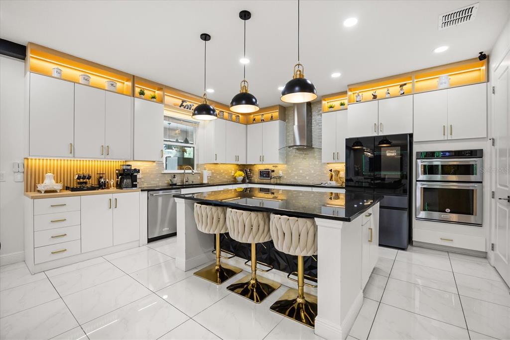 A modern kitchen features white cabinetry, a black island with bar stools, and gold accents — 8109 LUDINGTON CIRCLE, ORLANDO, FL