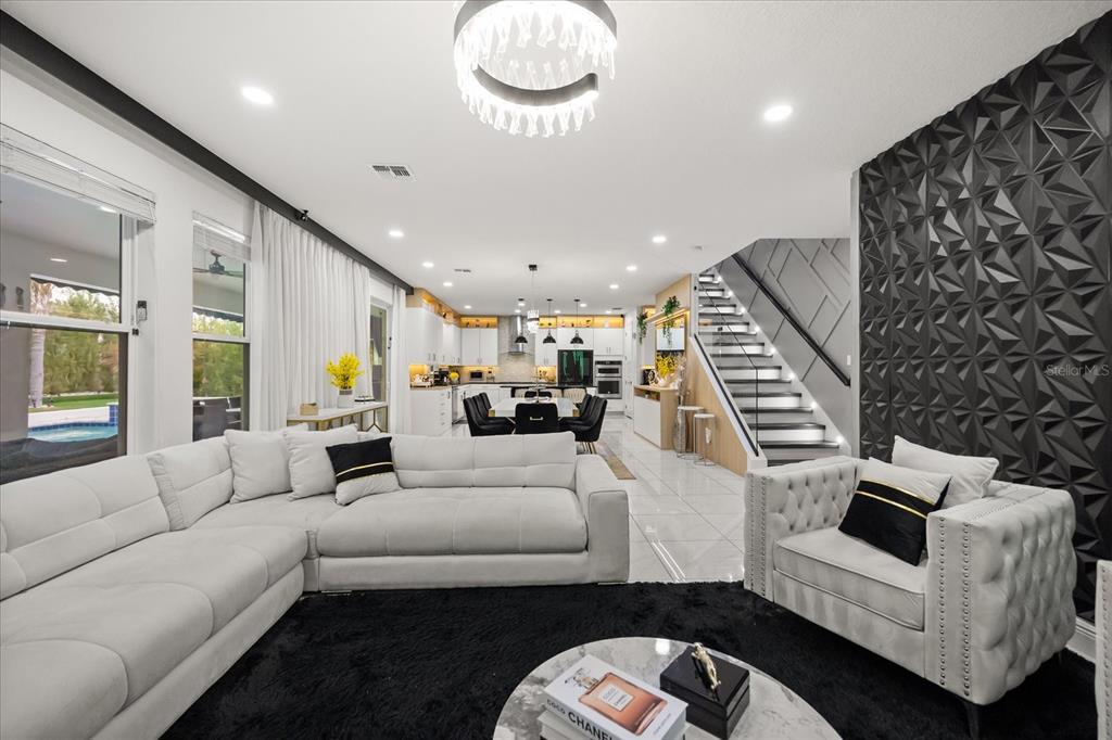 A modern open-concept living room features a white sectional, tufted armchair, and a textured black wall — 8109 LUDINGTON CIRCLE, ORLANDO, FL