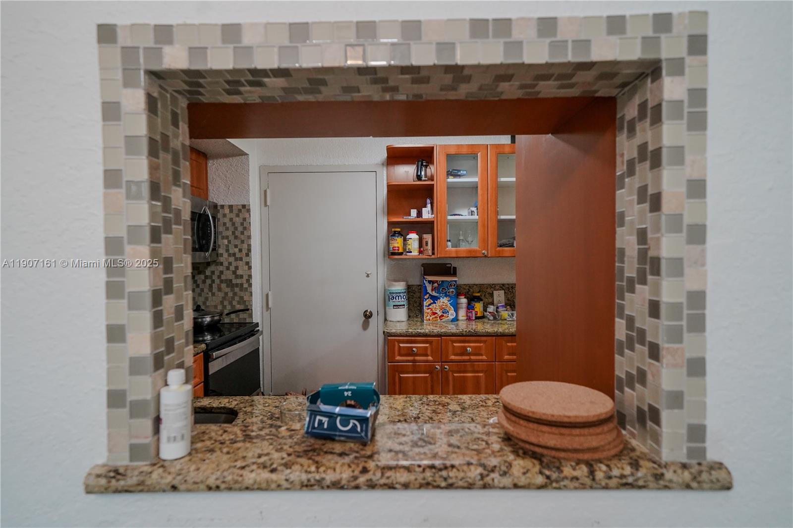 A kitchen is viewed through a tiled pass-through window with a granite countertop — 9125 SW 77th Ave # 103, Miami FL 33156, MIAMI, FL