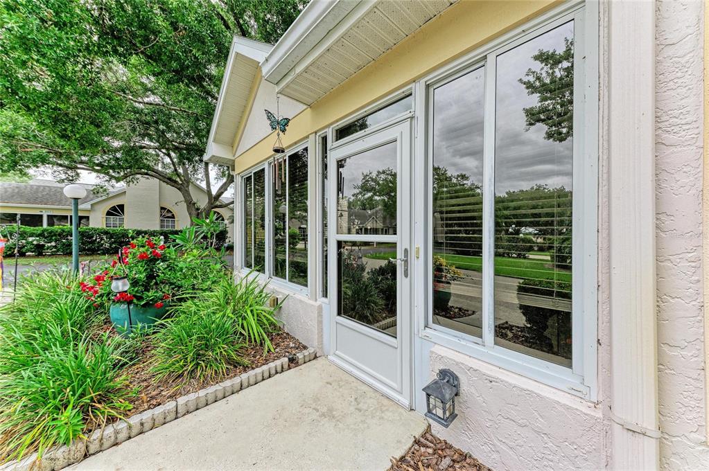A white storm door leads into a sunroom with large windows and a concrete walkway — 4512 CITATION LANE UNIT D, SARASOTA, FL