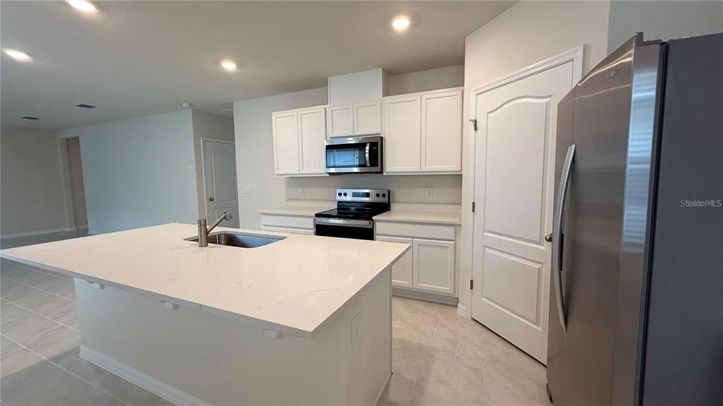A kitchen features white cabinets, stainless steel appliances, and a large quartz-topped island — 3314 PINE LILY AVENUE, POINCIANA, FL