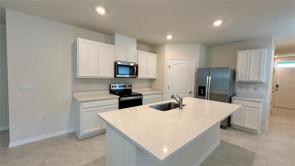 A kitchen features white cabinets, stainless steel appliances, a center island, and light-colored tile flooring — 3314 PINE LILY AVENUE, POINCIANA, FL