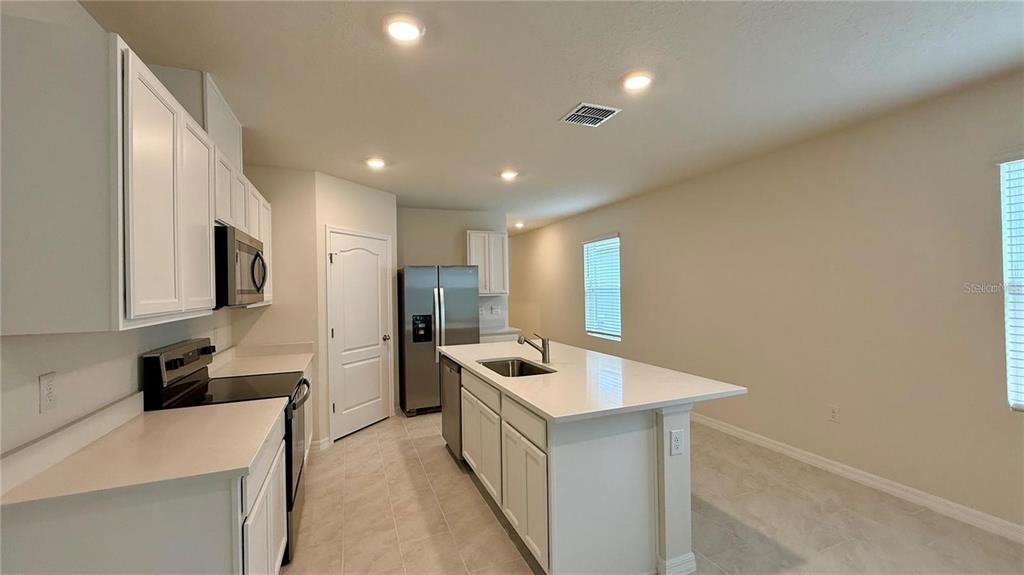A kitchen features white cabinets, stainless steel appliances, a center island, and tile flooring — 3314 PINE LILY AVENUE, POINCIANA, FL
