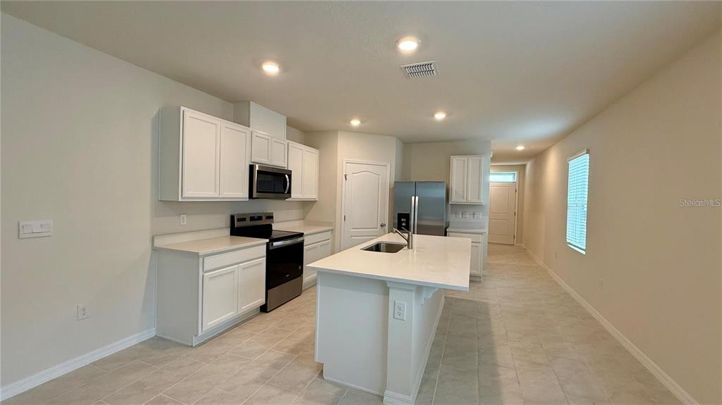 A modern kitchen features white cabinetry, stainless steel appliances, and a central island with seating — 3314 PINE LILY AVENUE, POINCIANA, FL