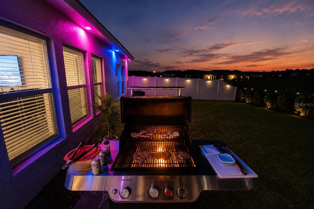 A Char-Broil grill sits on a patio at sunset with colorful exterior accent lighting — 792 REGGIE ROAD, WINTER HAVEN, FL