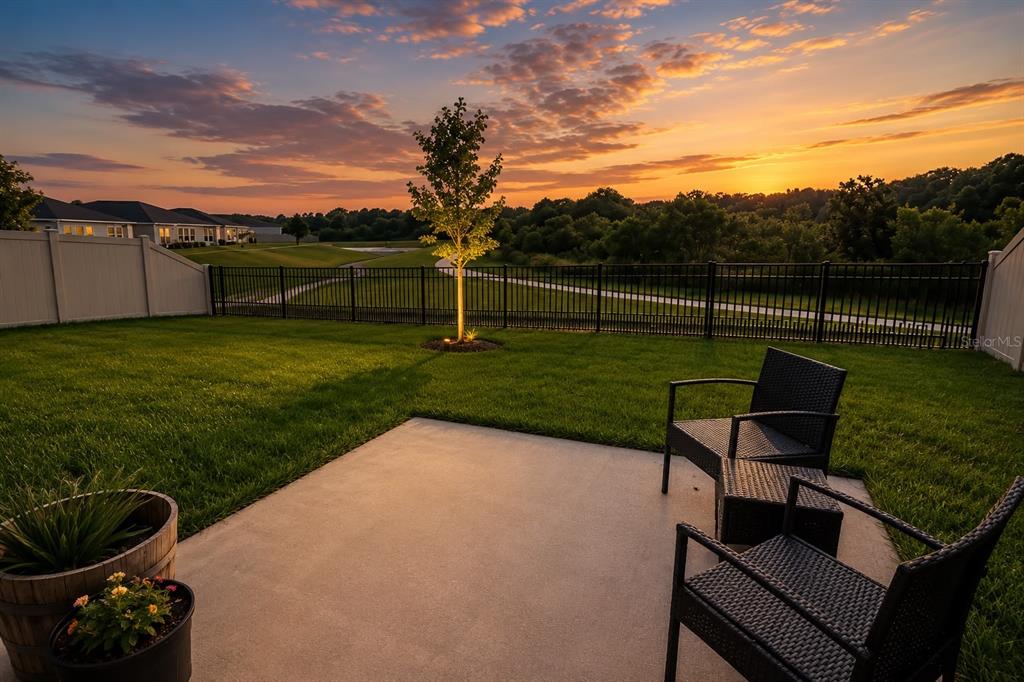 A concrete patio with outdoor furniture overlooks a grassy backyard, a fence, and a sunset — 792 REGGIE ROAD, WINTER HAVEN, FL