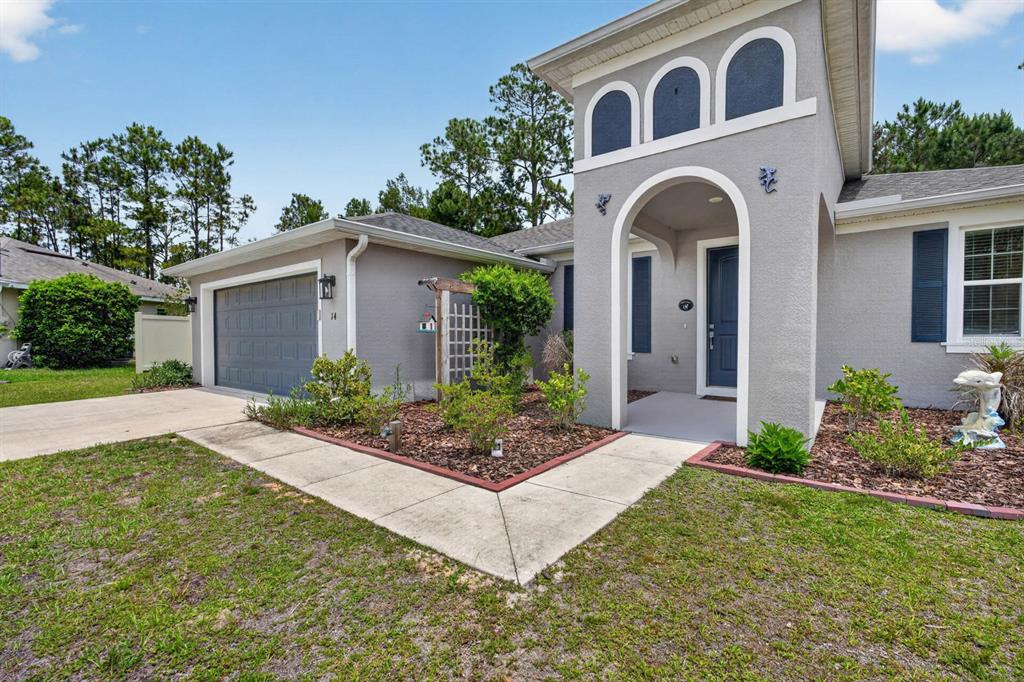 A gray house with a blue garage door, arched entryway, and a concrete walkway — 14 SEVILLE PLACE, PALM COAST, FL