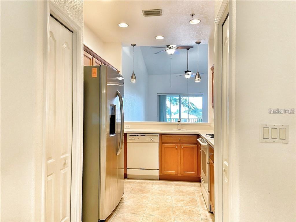 A kitchen with stainless steel appliances, wood cabinets, and tile flooring opens to a living area — 915 FAIRWAYCOVE LANE UNIT 208, BRADENTON, FL