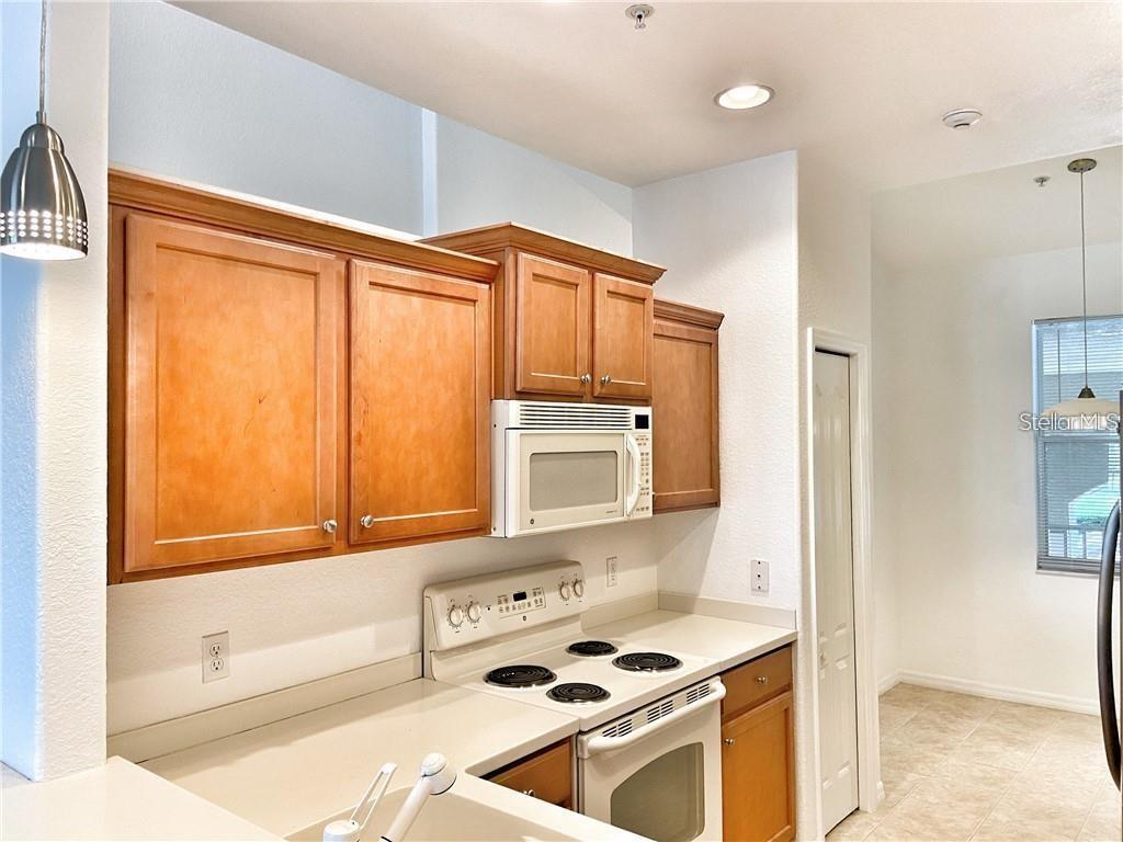 A kitchen features wooden cabinets, a white microwave, a white stove, and light countertops — 915 FAIRWAYCOVE LANE UNIT 208, BRADENTON, FL