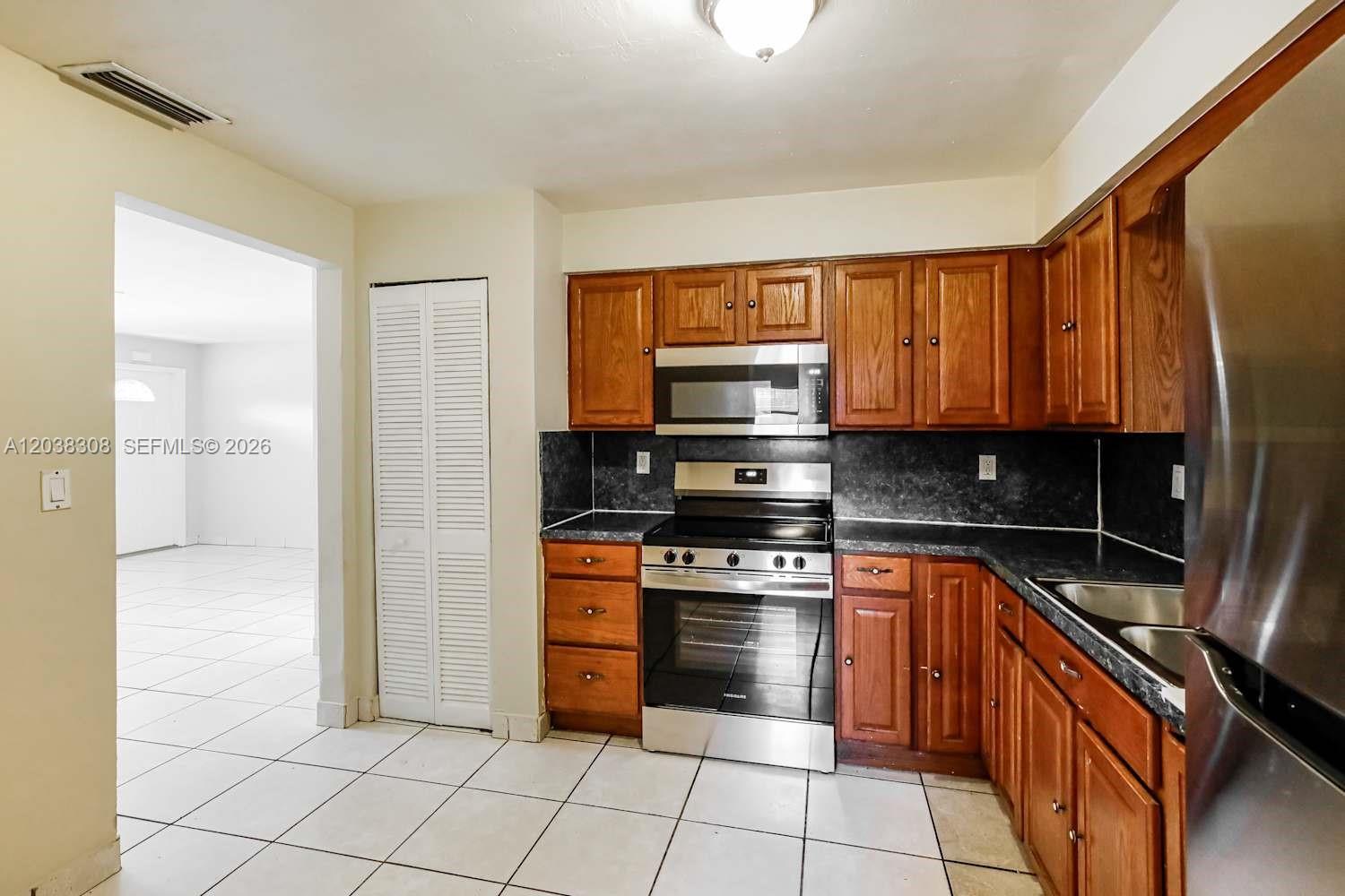 A kitchen features wood cabinets, stainless steel appliances, dark countertops, and white tile flooring — FORT LAUDERDALE, FL