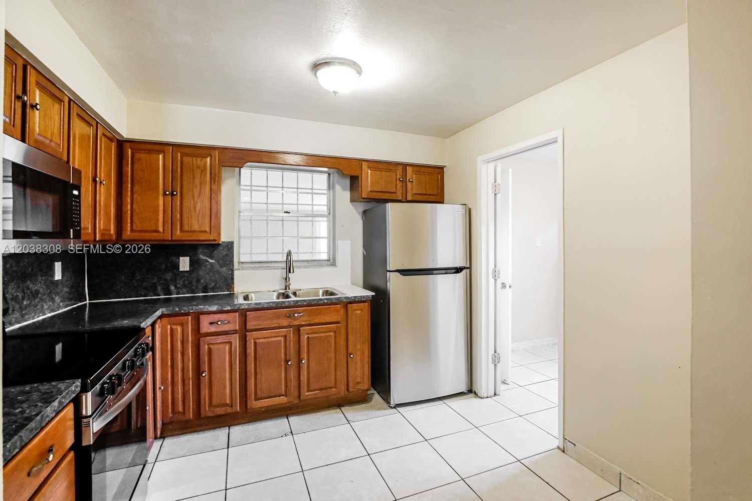 A kitchen features wood cabinets, stainless steel appliances, dark countertops, and white tile flooring — FORT LAUDERDALE, FL