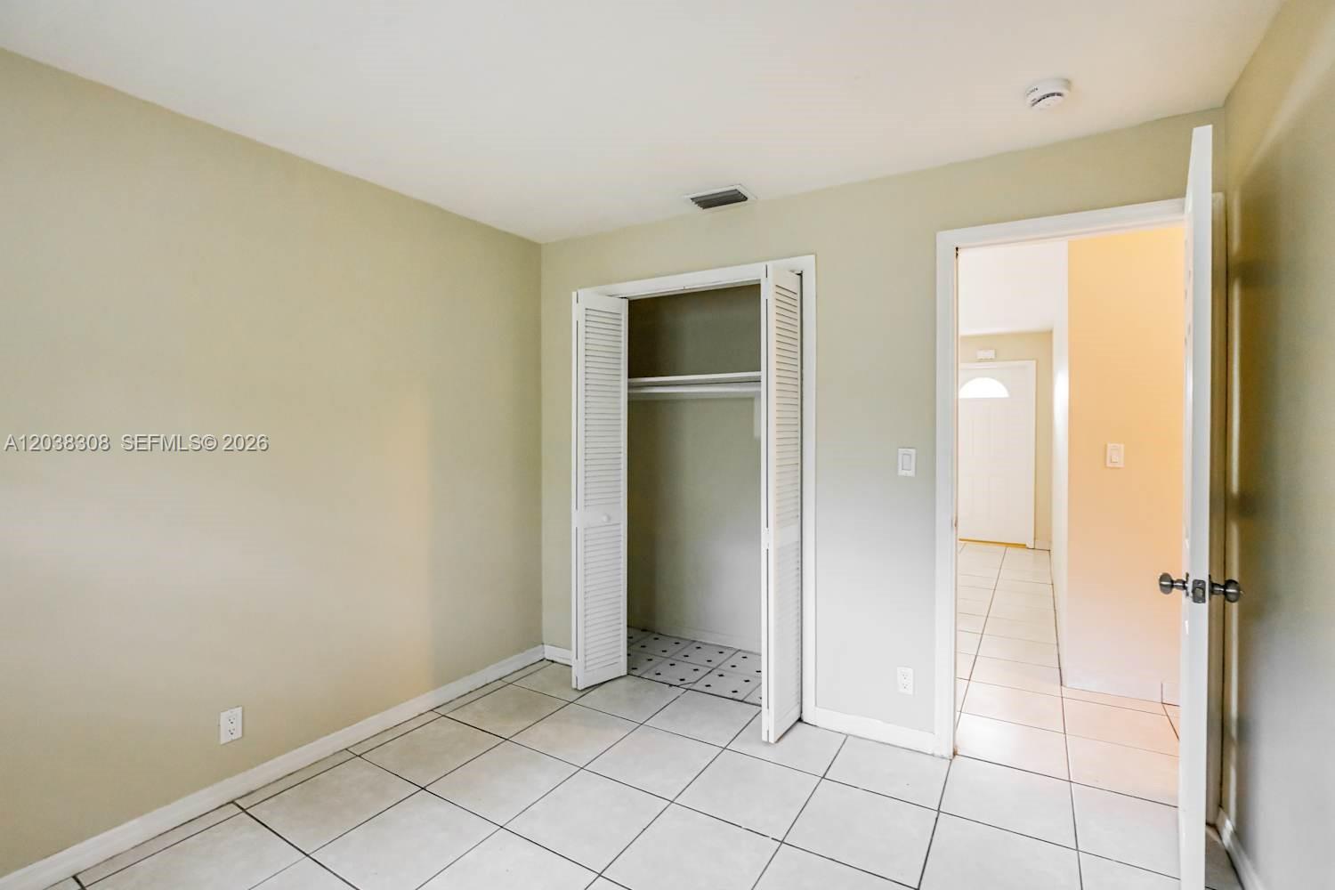 A bedroom features light-colored walls, white tile flooring, and an open louvered-door closet — FORT LAUDERDALE, FL