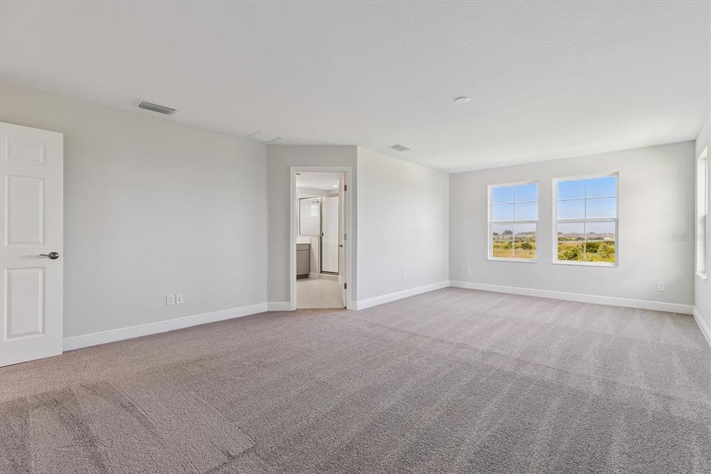 A spacious carpeted bedroom features light gray walls, two windows, and an attached bathroom doorway — 9711 SURREY ROSE DRIVE, SAN ANTONIO, FL