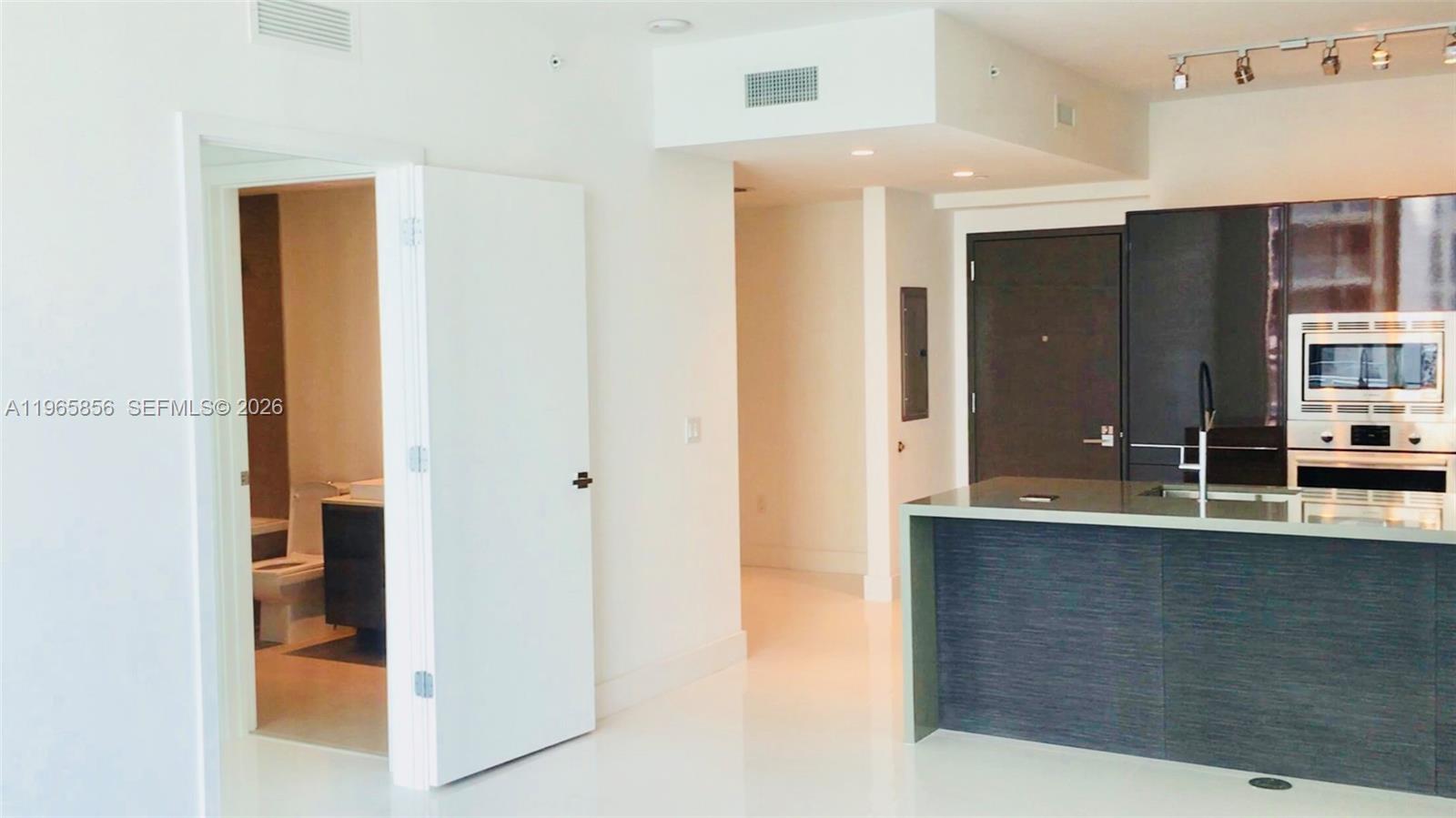 A modern kitchen with dark cabinetry and a white island opens into a hallway — 1080 Brickell Ave # 2607, Miami FL 33131, MIAMI, FL