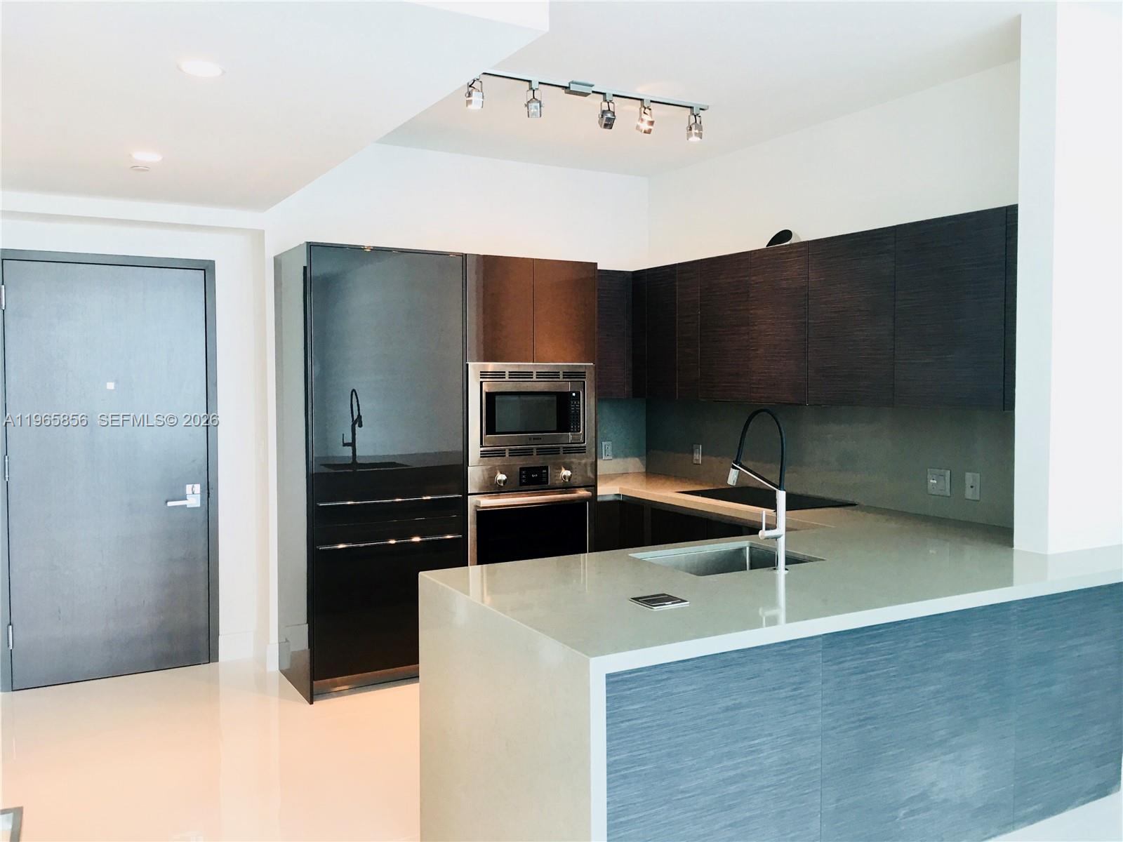 A modern kitchen features dark wood cabinetry, stainless steel appliances, and a light stone countertop — 1080 Brickell Ave # 2607, Miami FL 33131, MIAMI, FL
