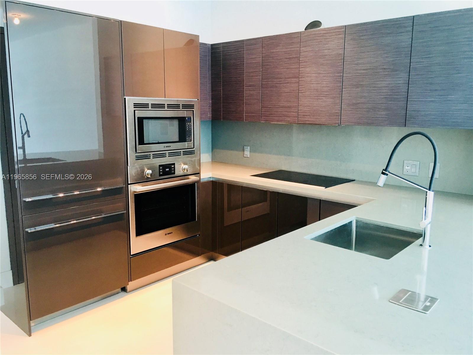 A modern kitchen features brown glossy cabinets, stainless steel appliances, and a white stone countertop — 1080 Brickell Ave # 2607, Miami FL 33131, MIAMI, FL