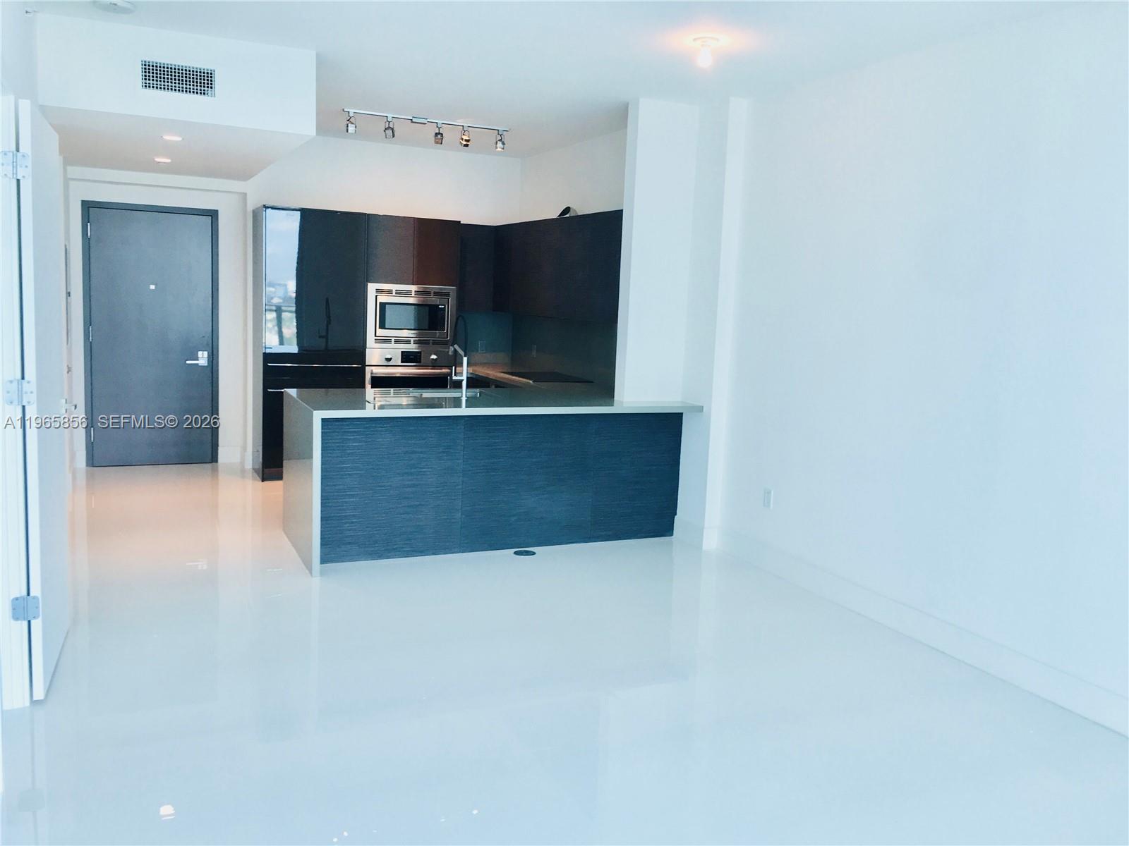 A modern kitchen features dark cabinetry, a breakfast bar, and glossy white floors — 1080 Brickell Ave # 2607, Miami FL 33131, MIAMI, FL